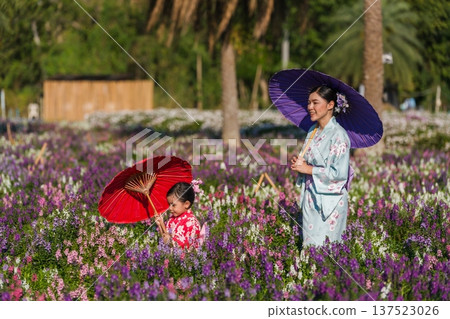 woman and child girl in yukata (kimono dress) walking with angelonia flower blooming in garden 137523026