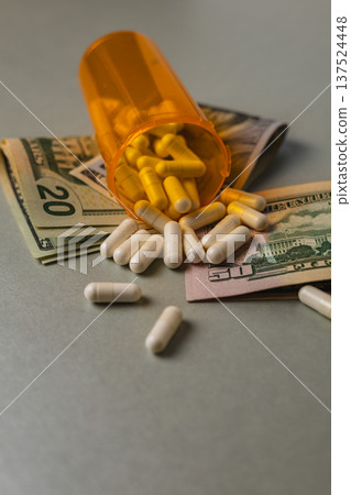 Pills spill from a bottle next to money on a plain surface Pills spill from a bottle next to money on a plain surface 137524448