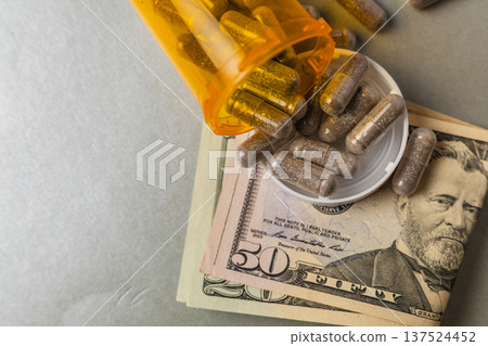 Pill bottle spills capsules over a fifty dollar bill on a table 137524452