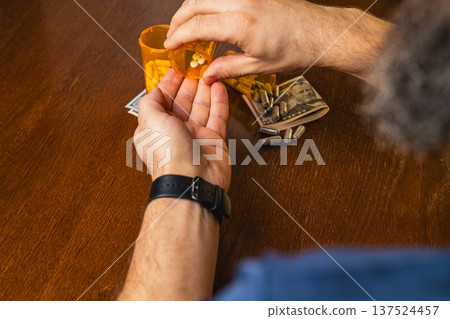 Man holds pills in hand with a prescription bottle and money on table Man holds pills in hand with a prescription bottle and money on table 137524457