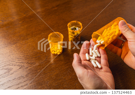 Holding white pills from a container while two other pill bottles are visible Holding white pills from a container while two other pill bottles are visible 137524463