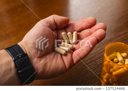 Person holds nutritional capsules in hand near a bottle on table Person holds nutritional capsules in hand near a bottle on table 137524466