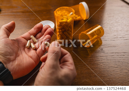 Handling capsules from prescription bottles on a wooden table Handling capsules from prescription bottles on a wooden table 137524468