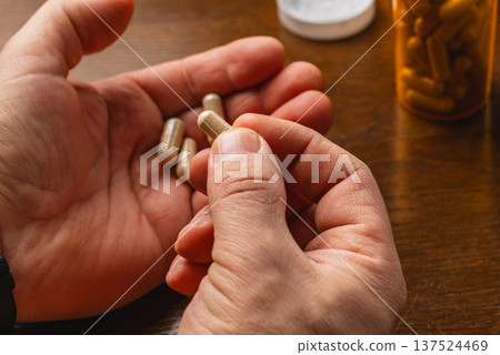 Person holds a supplement capsule above other capsules on a wooden table Person holds a supplement capsule above other capsules on a wooden table 137524469