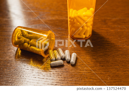 Pills spilled from two bottles on a wooden table during daytime Pills spilled from two bottles on a wooden table during daytime 137524470