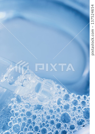 Clear cosmetic liquid dripping from dropper onto blue water bubbles, symbolizing skincare treatment Clear cosmetic liquid dripping from dropper onto blue water bubbles, symbolizing skincare treatment 137524654