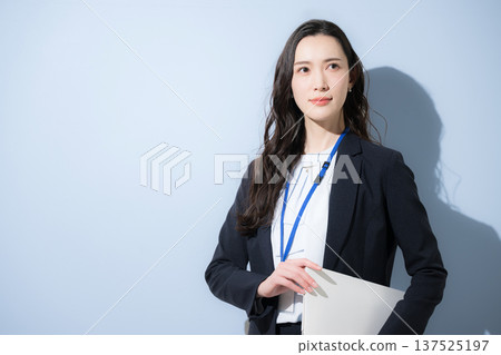 A cool woman in a business suit wearing a name tag and holding a laptop against a light blue background. Image of looking up at the future and goals. A cool woman in a business suit wearing a name tag and holding a laptop against a light blue background. Image of looking up at the future and goals. 137525197