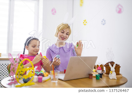 A mother and daughter enjoy decorating Easter eggs together while participating in an online class, fostering family bonding and festive creativity A mother and daughter enjoy decorating Easter eggs together while participating in an online class, fostering family bonding and festive creativity 137526467