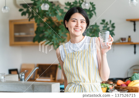 A young Asian woman wearing an apron hydrating in the kitchen A young Asian woman wearing an apron hydrating in the kitchen 137526715