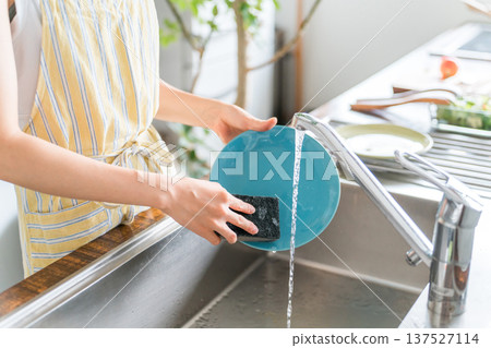 一位身穿圍裙的女性/家庭主婦正在洗碗。 137527114