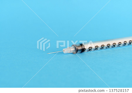Medical insulin syringe with needle isolated on a vibrant blue background. A close-up studio shot of a sterile disposable syringe used for injections, healthcare, and diabetes treatment. Medical insulin syringe with needle isolated on a vibrant blue background. A close-up studio shot of a sterile disposable syringe used for injections, healthcare, and diabetes treatment. 137528157