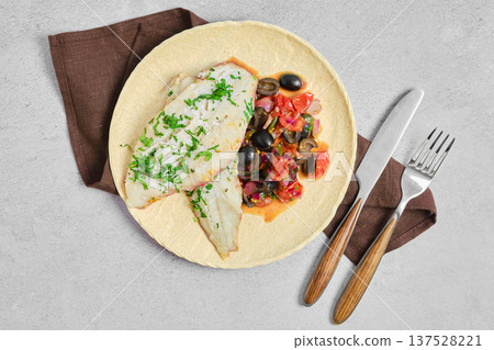 Fish dish with vegetables served on a plate with cutlery on a gray table in a simple setting Fish dish with vegetables served on a plate with cutlery on a gray table in a simple setting 137528221