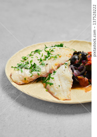 Fish with herbs served on a plate with olives and vegetables at a restaurant 137528222