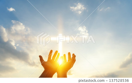 Human hands reaching up to a glowing cross in the sky. Concept of faith, hope, christianity, spirituality, divine light, blessing, and religious belief. Human hands reaching up to a glowing cross in the sky. Concept of faith, hope, christianity, spirituality, divine light, blessing, and religious belief. 137528536