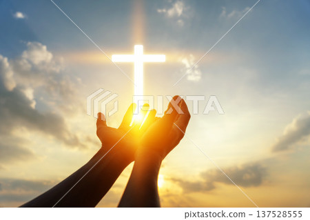 Human hands open palm up worshiping a glowing Christian cross in sunset sky. Concept for faith, spirituality, and hope. Human hands open palm up worshiping a glowing Christian cross in sunset sky. Concept for faith, spirituality, and hope. 137528555