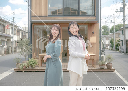 Two women standing back to back in front of a cafe Two women standing back to back in front of a cafe 137529399
