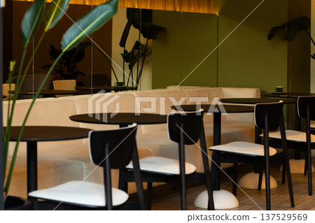 Modern cafe interior with black tables, white chairs, and beige banquette seating 137529569