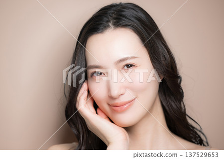 A beauty image of a young woman with beautiful black hair and a glossy, translucent look against a beige background, looking at the camera, close-up A beauty image of a young woman with beautiful black hair and a glossy, translucent look against a beige background, looking at the camera, close-up 137529653
