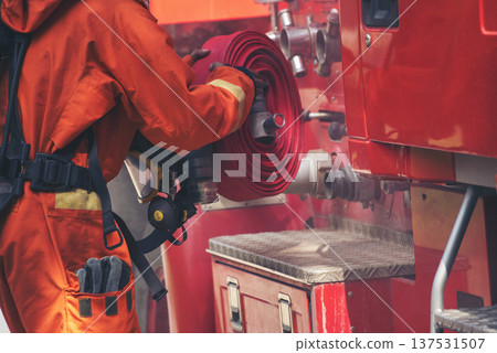 Fireman prepare equipment fighting extinguisher at fire engine truck. Firefighter fighting with smoke flame using fire hose, tube, chemical water foam spray at truck. Fireman wear hard hat protection Fireman prepare equipment fighting extinguisher at fire engine truck. Firefighter fighting with smoke flame using fire hose, tube, chemical water foam spray at truck. Fireman wear hard hat protection 137531507
