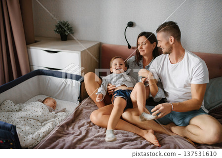 Loving Parents Playing With Son Beside Sleeping Baby Loving Parents Playing With Son Beside Sleeping Baby 137531610
