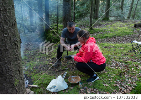 Couple preparing a meal in a serene forest setting during golden hour with soft light filtering through trees Couple preparing a meal in a serene forest setting during golden hour with soft light filtering through trees 137532038