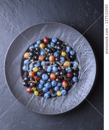Blueberries, gooseberry and mulberries in dark ceramic bowl 137532095