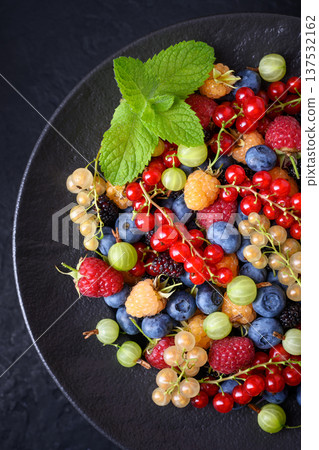 Mixed summer berries in dark plate with mint leaves Mixed summer berries in dark plate with mint leaves 137532162
