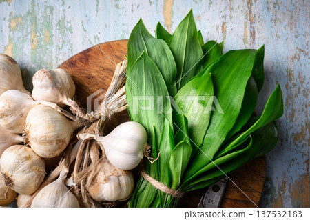 Wild garlic leaves with bundle of garlic bulbs placed on wooden cutting board Wild garlic leaves with bundle of garlic bulbs placed on wooden cutting board 137532183