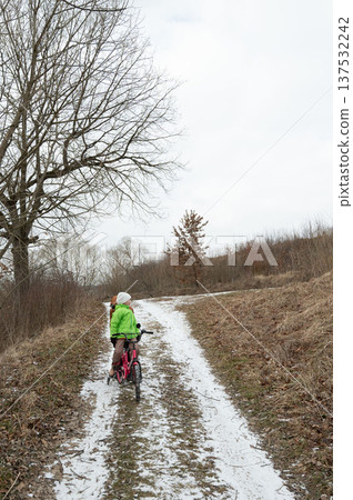 Riding a bicycle through a snowy trail on a chilly winter day in a serene landscape filled with bare trees and soft earth tones 137532242