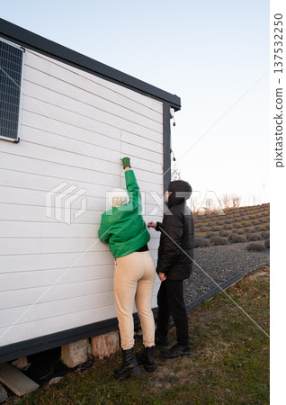 Creative renovation at sunset as two individuals collaborate to paint details on a cozy, modern cabin in a serene rural setting 137532250