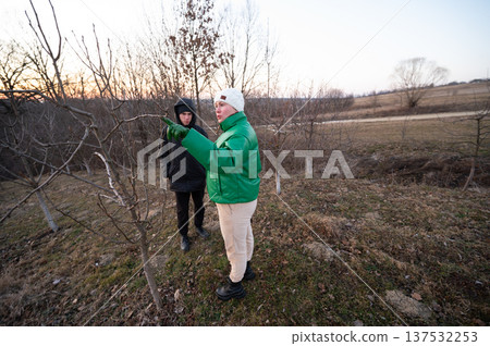 Discussion on tree care during early evening by two individuals in a rural landscape with winter hues and a fading sunset in the background Discussion on tree care during early evening by two individuals in a rural landscape with winter hues and a fading sunset in the background 137532253