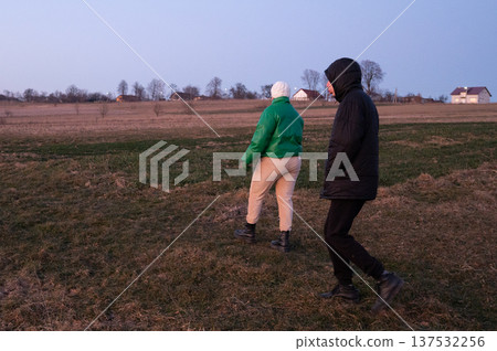 Couple strolls through the tranquil countryside at dusk, embracing the quiet moments as the day transitions into night and soft hues of twilight fill the sky Couple strolls through the tranquil countryside at dusk, embracing the quiet moments as the day transitions into night and soft hues of twilight fill the sky 137532256