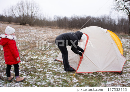 Organizing a thrilling winter camping adventure with a child amidst a picturesque snowy landscape, where the trees stand bare and silent Organizing a thrilling winter camping adventure with a child amidst a picturesque snowy landscape, where the trees stand bare and silent 137532533