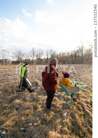 Children playing outdoors in a sunny field while being pushed in a wheelbarrow by a parent during a bright afternoon in early spring 137532540