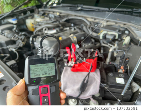 Man is measuring AGM battery power of suv car by battery tester at home. 137532581