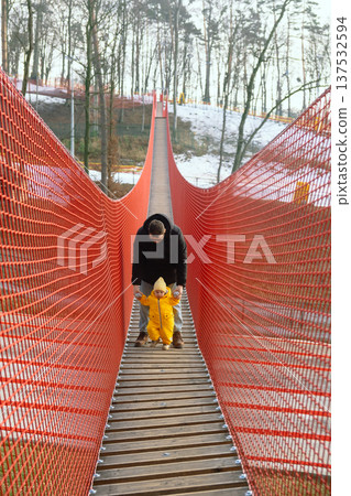 Father holding toddler on red suspension bridge in winter forest Father holding toddler on red suspension bridge in winter forest 137532594