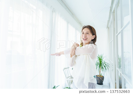 一位中年日本婦女在窗邊伸展身體 一位中年日本婦女在窗邊伸展身體 137532663