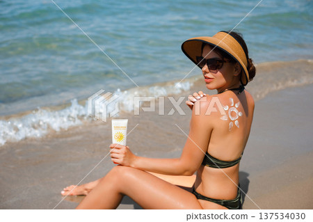 Beautiful woman relaxing at seaside with sunscreen lotion and suncream sun pattern on her back Beautiful woman relaxing at seaside with sunscreen lotion and suncream sun pattern on her back 137534030