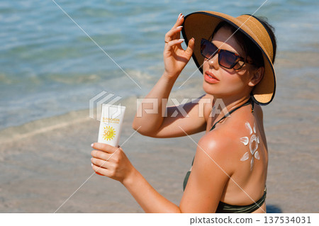 Woman with sunscreen lotion showing suncream sun pattern on her back during beach holiday Woman with sunscreen lotion showing suncream sun pattern on her back during beach holiday 137534031