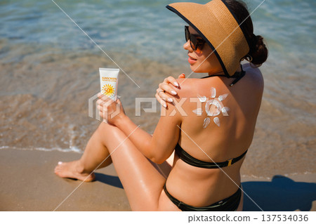 Beautiful woman relaxing at seaside with sunscreen lotion and suncream sun pattern on her back Beautiful woman relaxing at seaside with sunscreen lotion and suncream sun pattern on her back 137534036