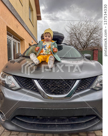 Toddler Sitting on Hood of Gray Suv in Driveway 137534330