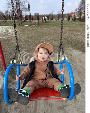 Smiling toddler on playground swing in outdoor park Smiling toddler on playground swing in outdoor park 137534354
