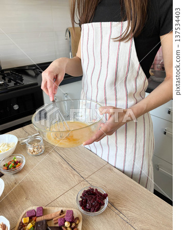 A young woman in the kitchen is preparing a pie, whisking eggs in a glass bowl 137534403