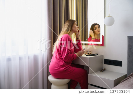 Young woman applying mascara at mirror vanity table 137535104