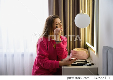 Young woman applying makeup at vanity mirror 137535107