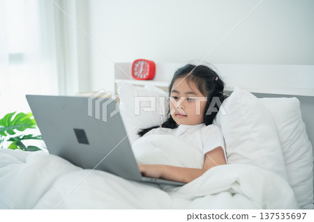 Girl in White Bed Using Laptop with Headphones, Relaxing in Cozy Room, Morning Time, Bright Natural Light, Soft Bedding, Focused Learning Experience Girl in White Bed Using Laptop with Headphones, Relaxing in Cozy Room, Morning Time, Bright Natural Light, Soft Bedding, Focused Learning Experience 137535697