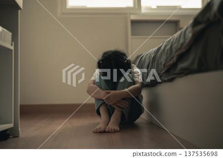 Emotional distress of a child sitting alone in a dimly lit room, showcasing vulnerability and isolation in a personal space, evoking feelings of sadness and fear. 137535698