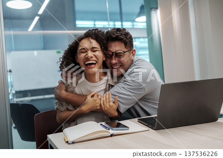 Happy Colleagues Share Warm Hug. Bright Office Scene Showcasing Genuine Emotion And Team Closeness Happy Colleagues Share Warm Hug. Bright Office Scene Showcasing Genuine Emotion And Team Closeness 137536226