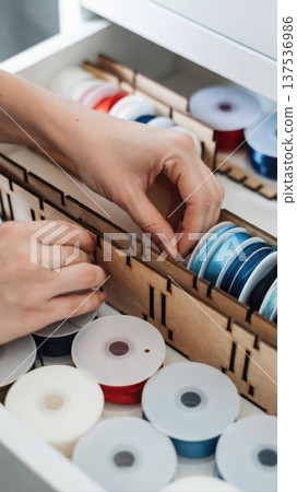 Adult Hands Organizing Ribbon Spools In Drawer 137536986