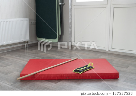 Red exercise mat with wooden staff and wrist weights in minimalist gym setting 137537523